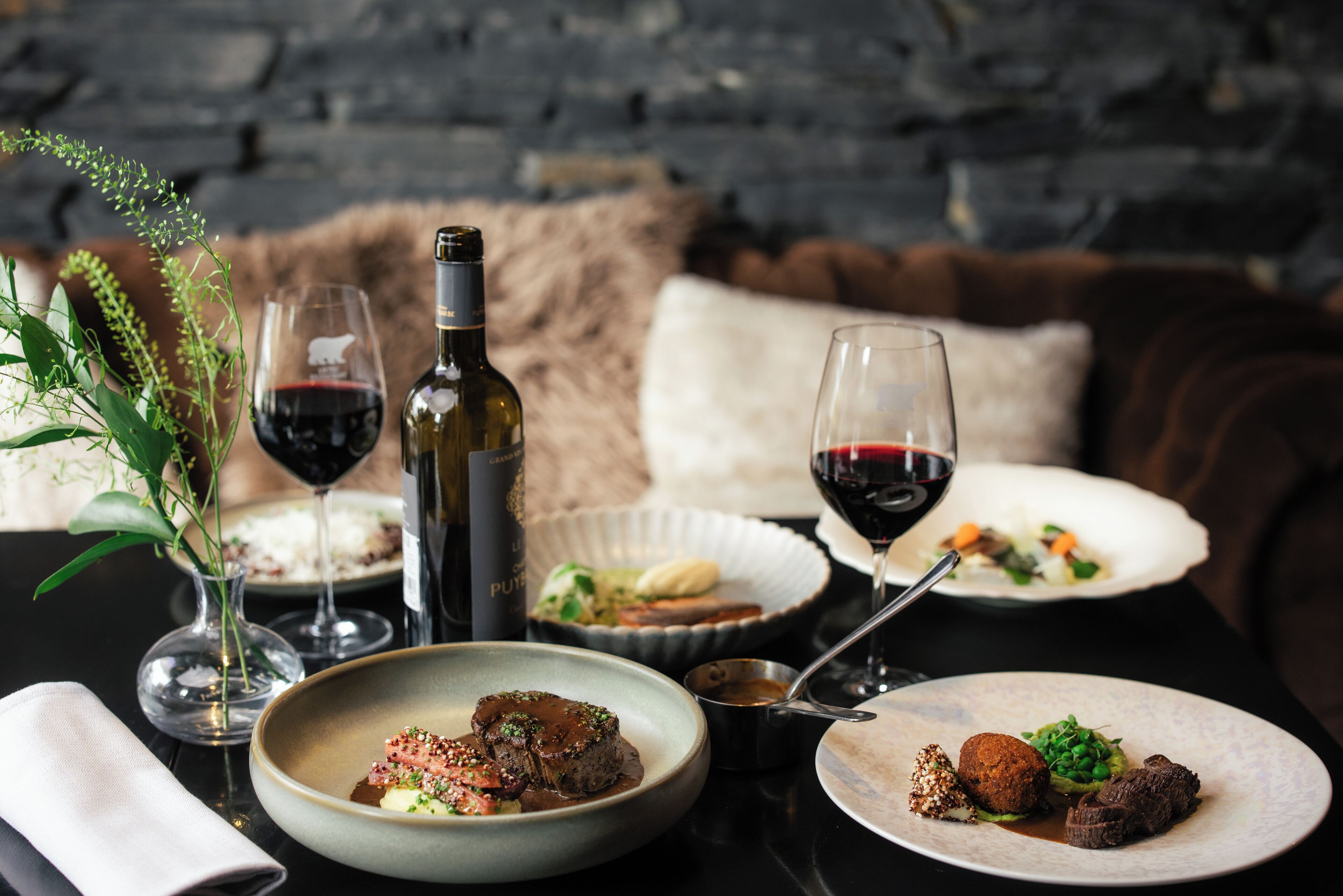 A dining table with plates of food, wine glasses, and a bottle of wine.