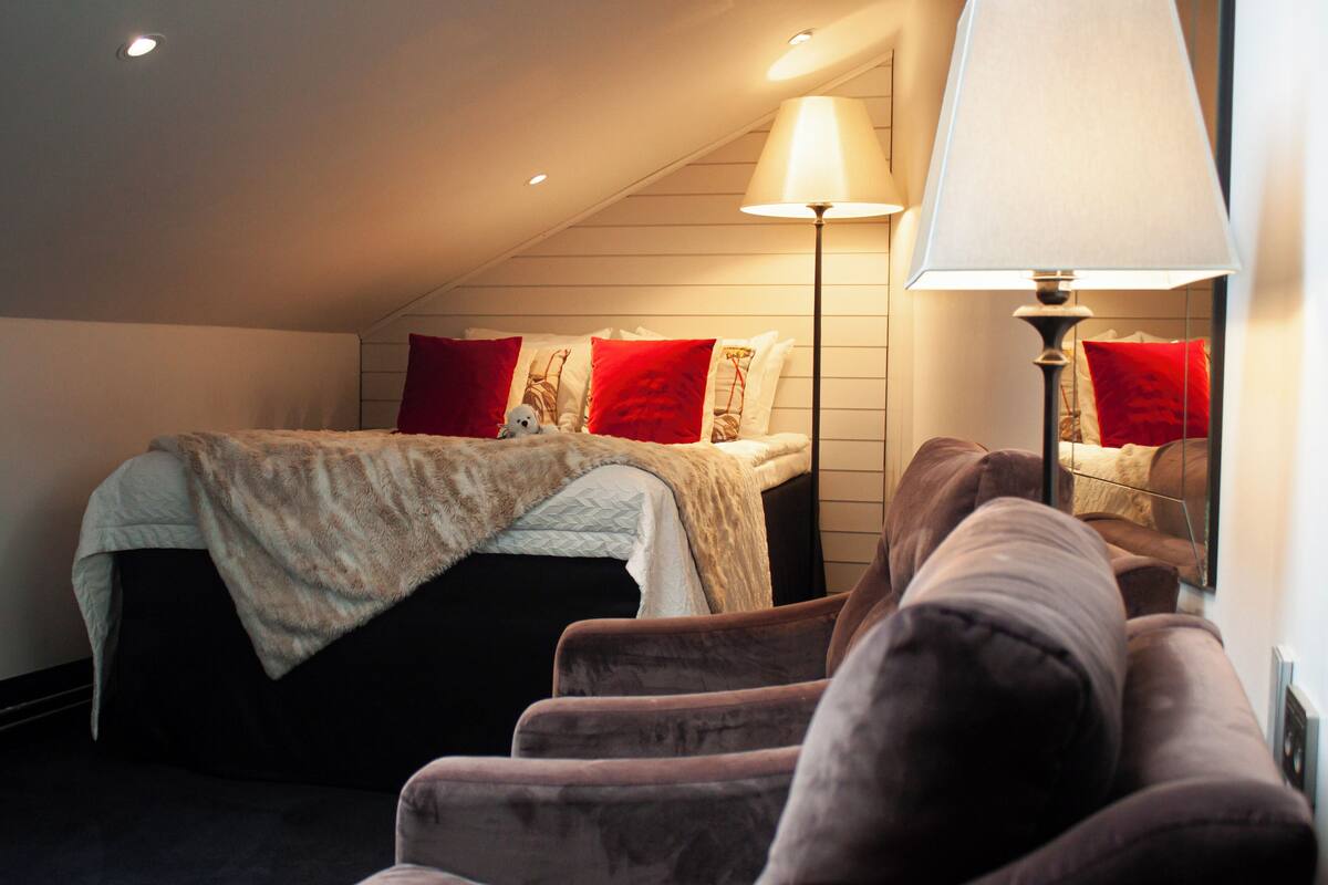 A bedroom with a bed, a red pillow, a lamp, and a couch.