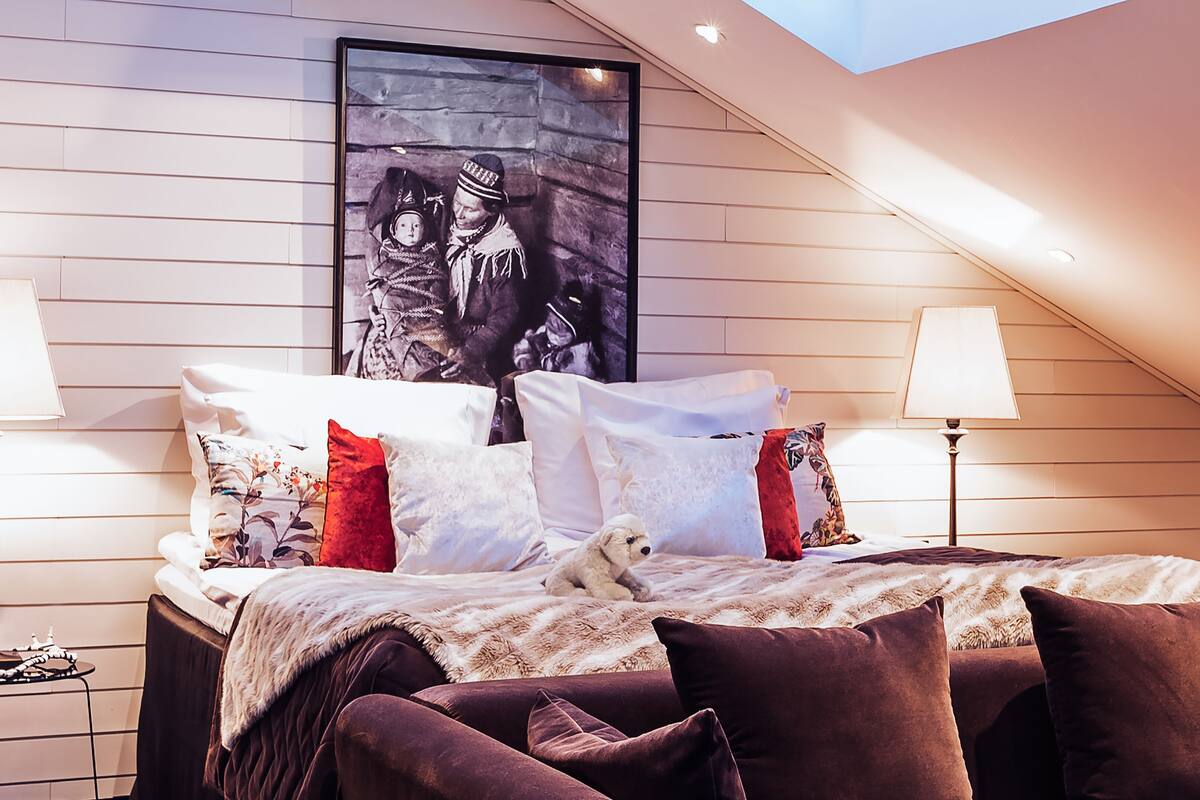A bedroom with a sloped ceiling, a bed with multiple pillows, a teddy bear, and a framed picture on the wall.