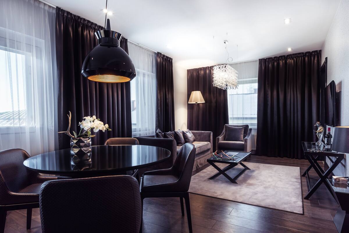 A modern living room with a round black table, leather chairs, a sofa, and a chandelier.