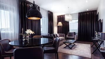 A modern living room with a round black table, leather chairs, a sofa, and a chandelier.