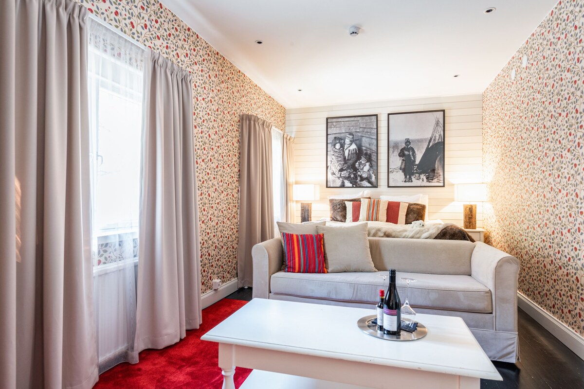 A living room with a sofa, a coffee table with a bottle and glass, and two framed pictures on the wall.