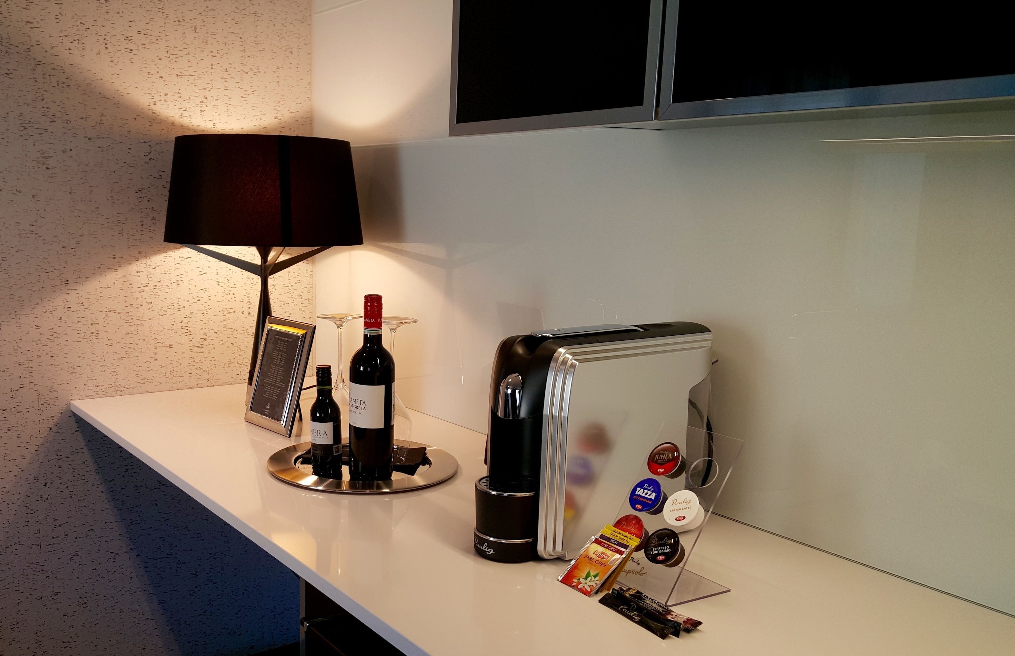 A kitchen counter with a wine bottle, a coffee maker, and a refrigerator with magnets.
