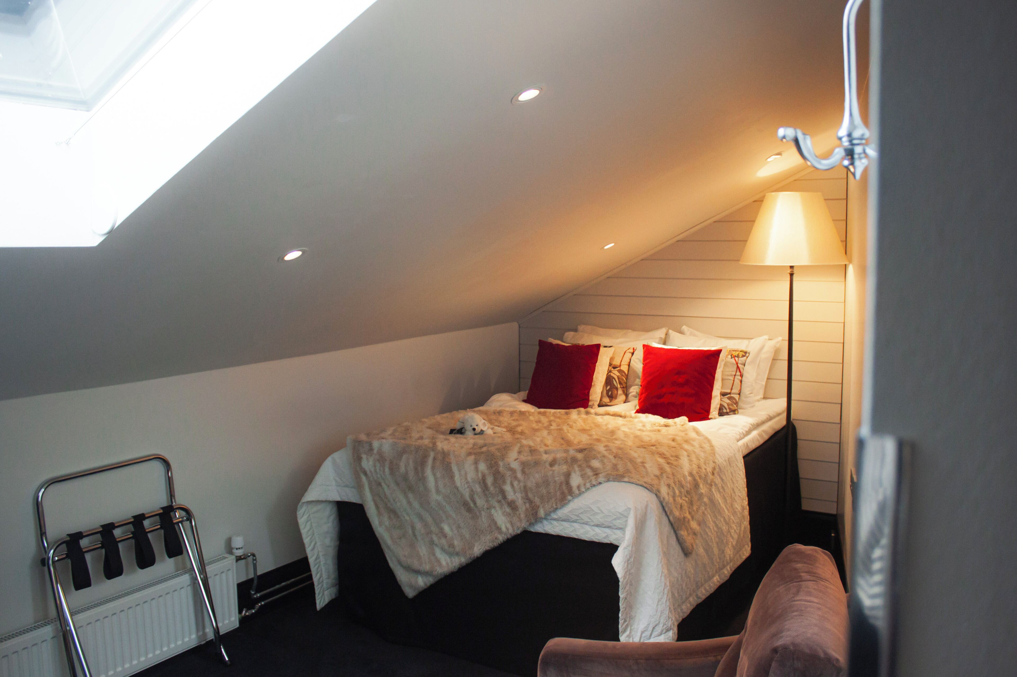 Ein Schlafzimmer mit Dachfenster, einem Bett mit Felldecke, roten Kissen, einer Nachttischlampe und einem Heizkörper.