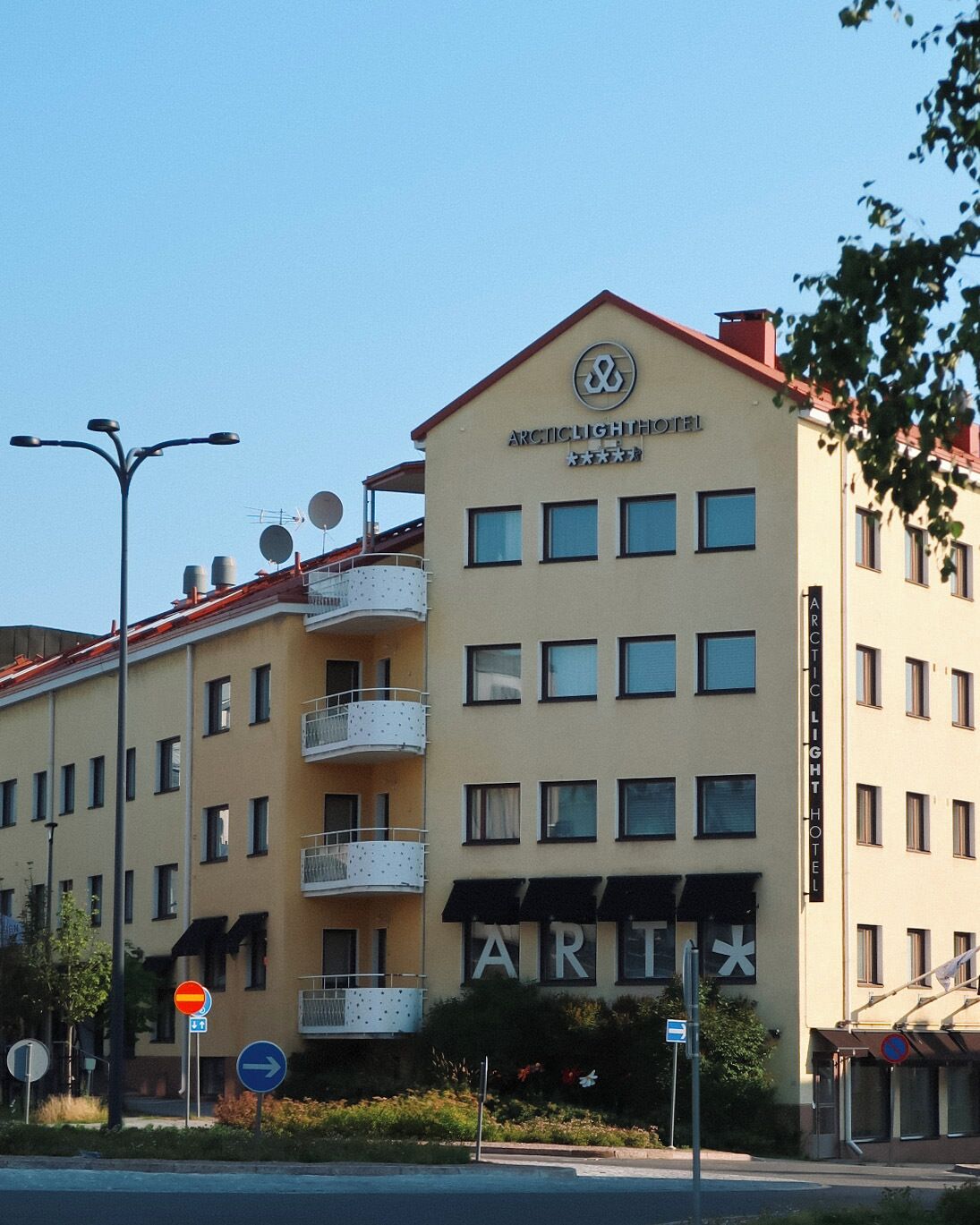 A multi-story building with balconies, a sign reading 'ARCIC LIGHT HOTEL,' and a sign for 'ART' below.