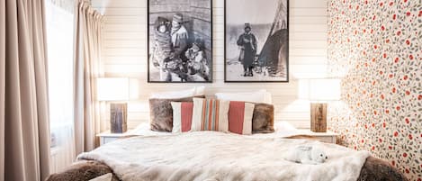 A bedroom with a large bed, two side tables, and two framed pictures on the wall.