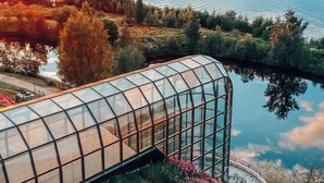Una estructura de invernadero con techo de vidrio curvo, rodeada por un jardín ajardinado con diversas plantas y flores.