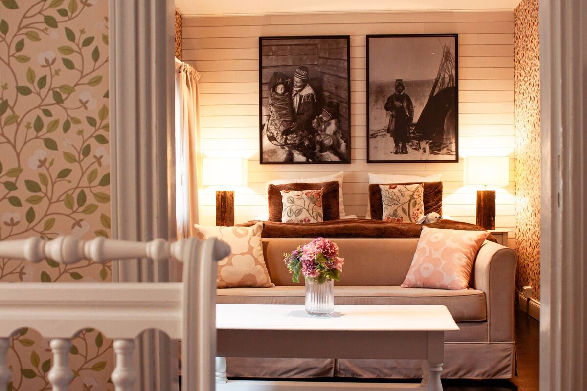 A room with a sofa, a table with a vase, and two framed pictures on the wall.