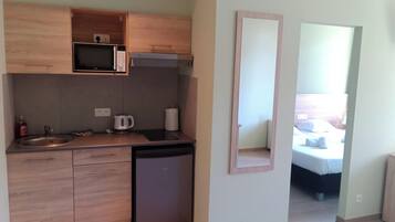 A compact kitchen with a microwave, kettle, and sink.