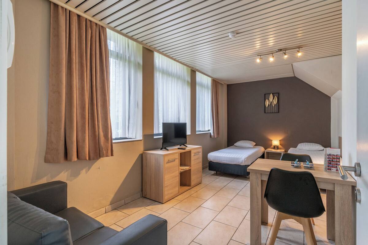 A modern hotel room with a wooden desk, a television, a bed, and a sofa.