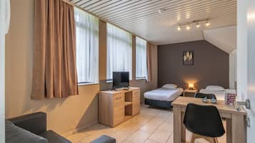 A modern hotel room with a wooden desk, a television, a bed, and a sofa.