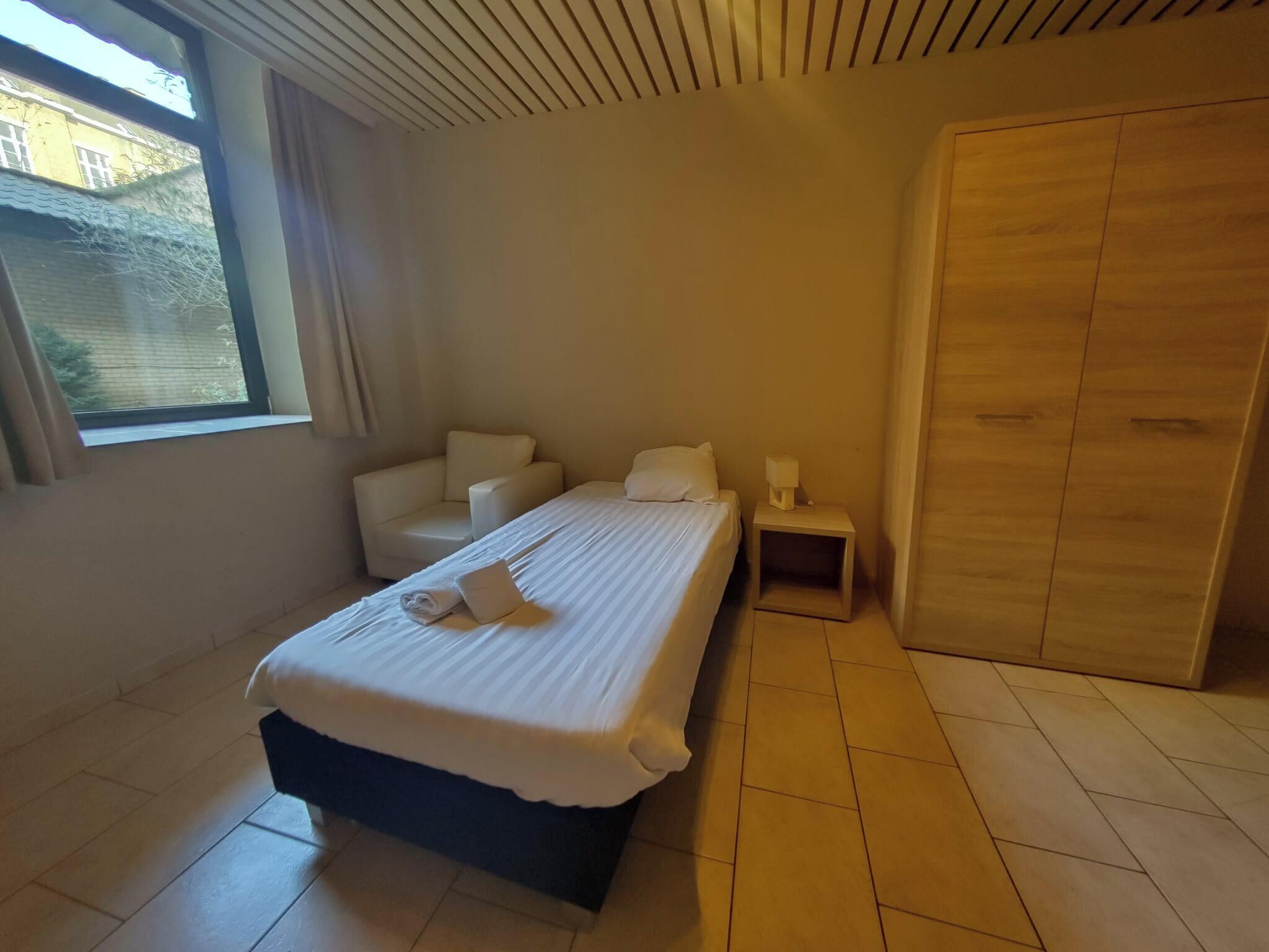 Habitación de hotel con cama, mesita de noche, armario y ventana.