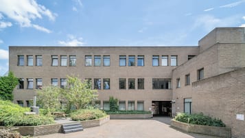 Un bâtiment moderne doté d’une cour intérieure, avec une façade en briques, de nombreuses fenêtres et quelques éléments de verdure.