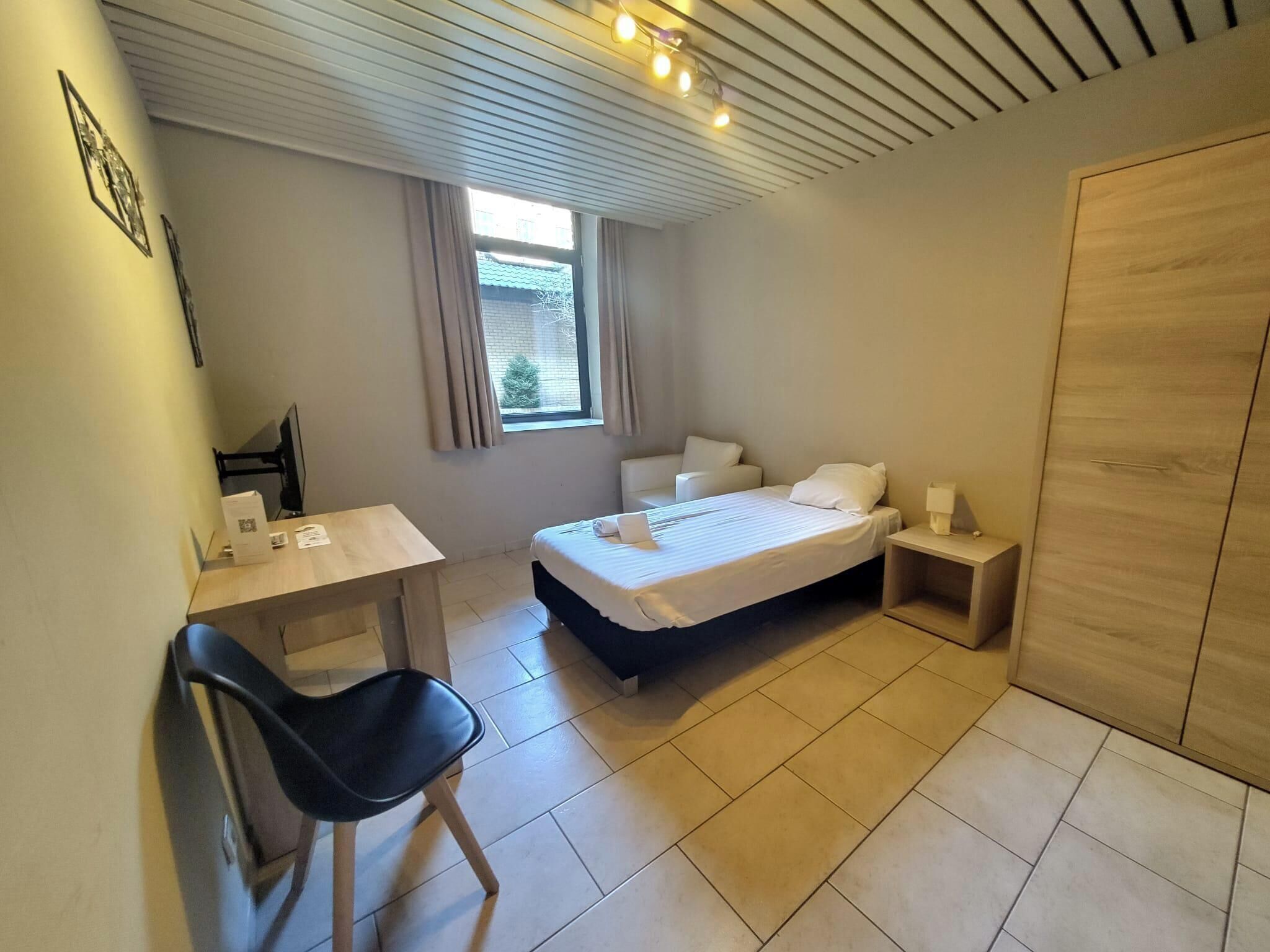 A small, clean room with a bed, a desk, a chair, and a wardrobe.