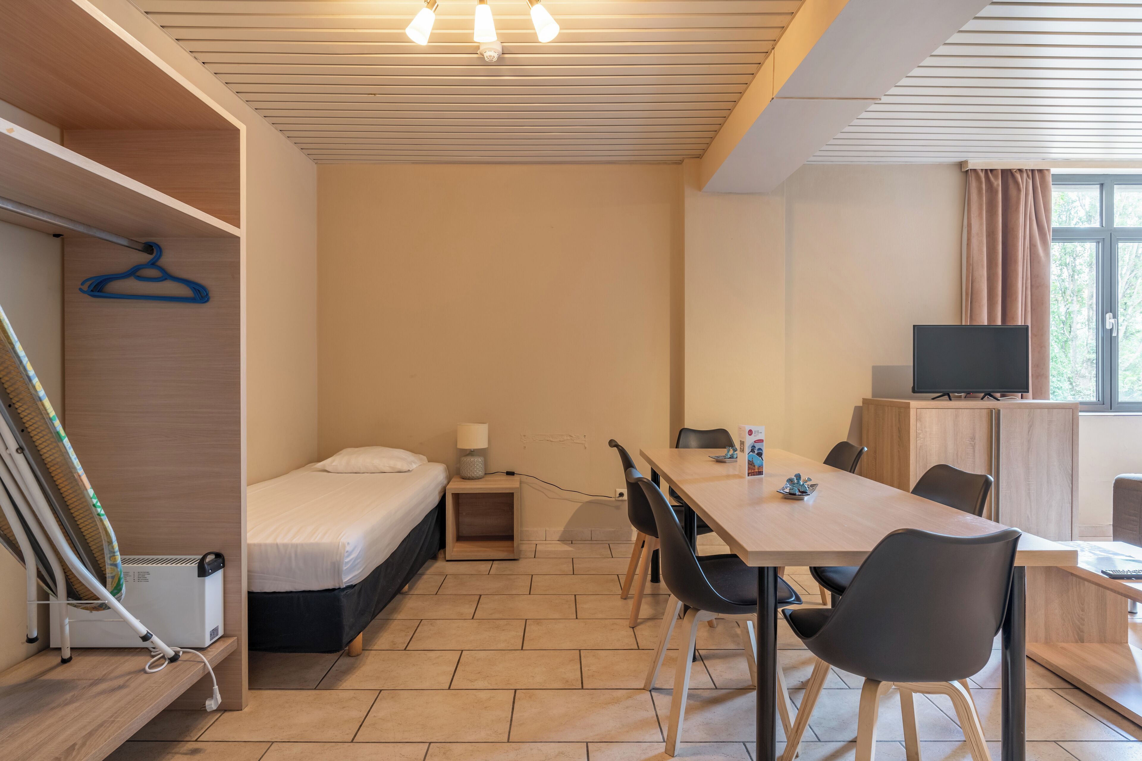 Habitación pequeña con cama, escritorio y televisor.