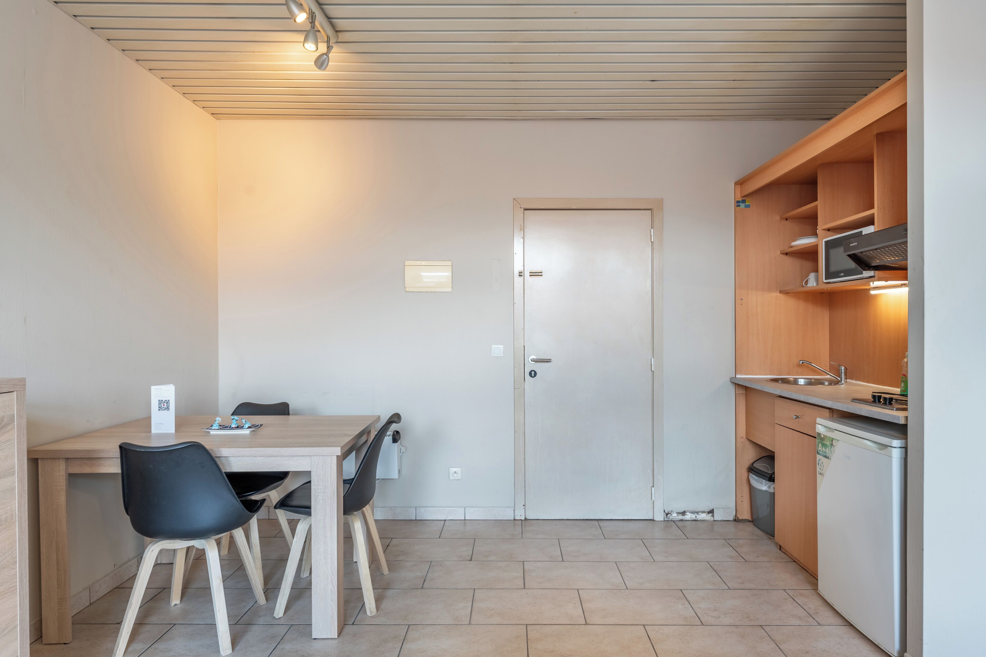 Una cocina compacta con comedor, una puerta y un pequeño cubo de basura.