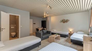 Una habitación moderna y bien iluminada con dos camas individuales, un sofá, una mesita y un baño con inodoro.