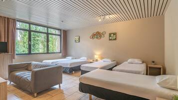 Une chambre d’hôtel avec un canapé, trois lits simples, une télévision et des œuvres d’art accrochées au mur.