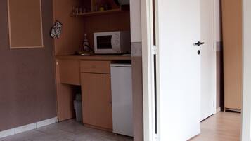 Een kleine keuken met een magnetron, kastjes en een spoelbak.