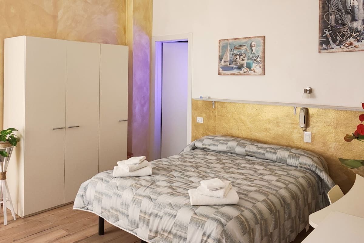 A bedroom with a bed, a wardrobe, a bedside table, a plant, and a painting on the wall.