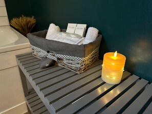 A bathroom with a wicker basket holding towels and toiletries, accompanied by a lit candle.