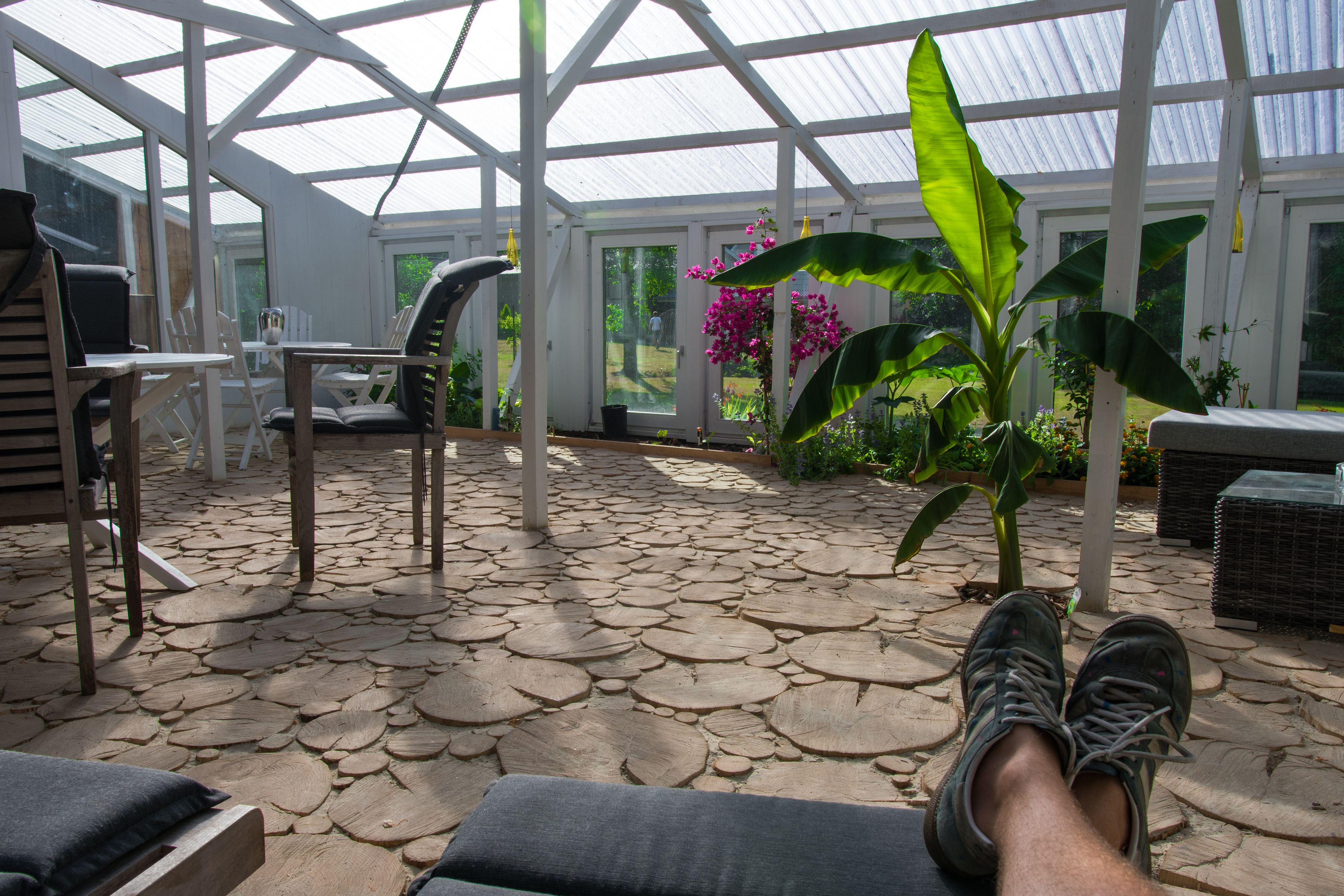 A conservatory with a stone-tiled floor, seating areas, and potted plants.