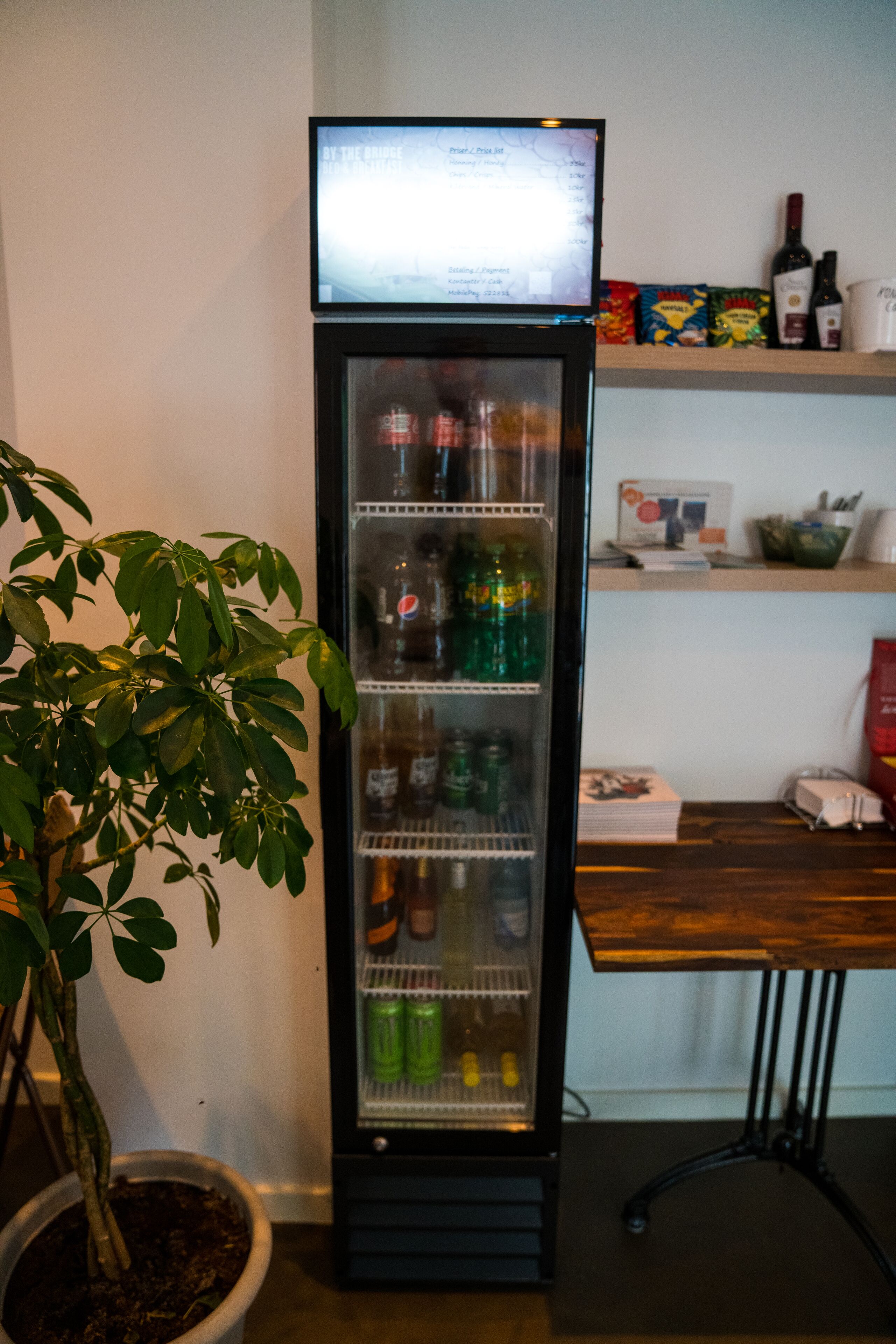 Un refrigerador lleno de bebidas, una planta en maceta y una mesa de madera con varios objetos.