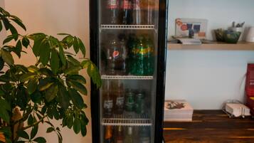 Un refrigerador lleno de bebidas, una planta en maceta y una mesa de madera con varios objetos.