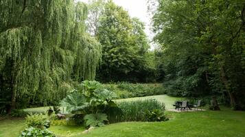 A lush garden with a pond, seating area, and various plants.