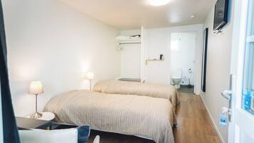 Una habitación de hotel con dos camas, un escritorio con lámpara, un televisor montado en la pared y un baño visible a través de una puerta abierta.