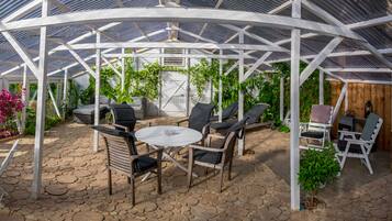 Ein überdachter Patio-Bereich mit Steinböden, weißen Holzkufen, einem runden Tisch und Blumentöpfen.