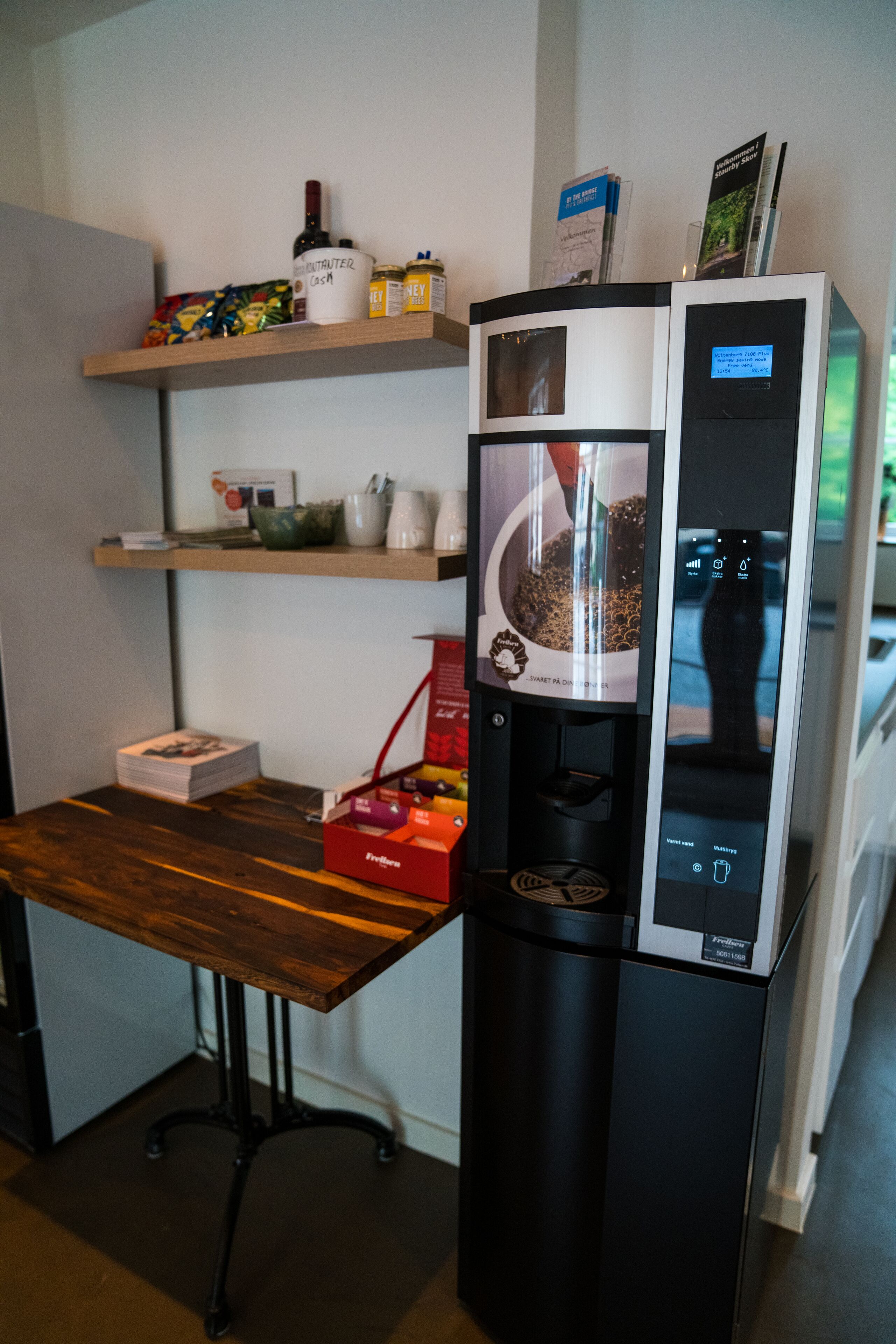 A coffee machine with a coffee pot, a milk frother, and a milk jug on a wooden table.