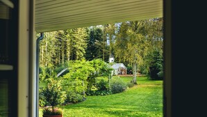 A view through a doorway of a lush garden with a small building and a tree.
