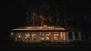 A house with a large porch and multiple windows, surrounded by a forest.