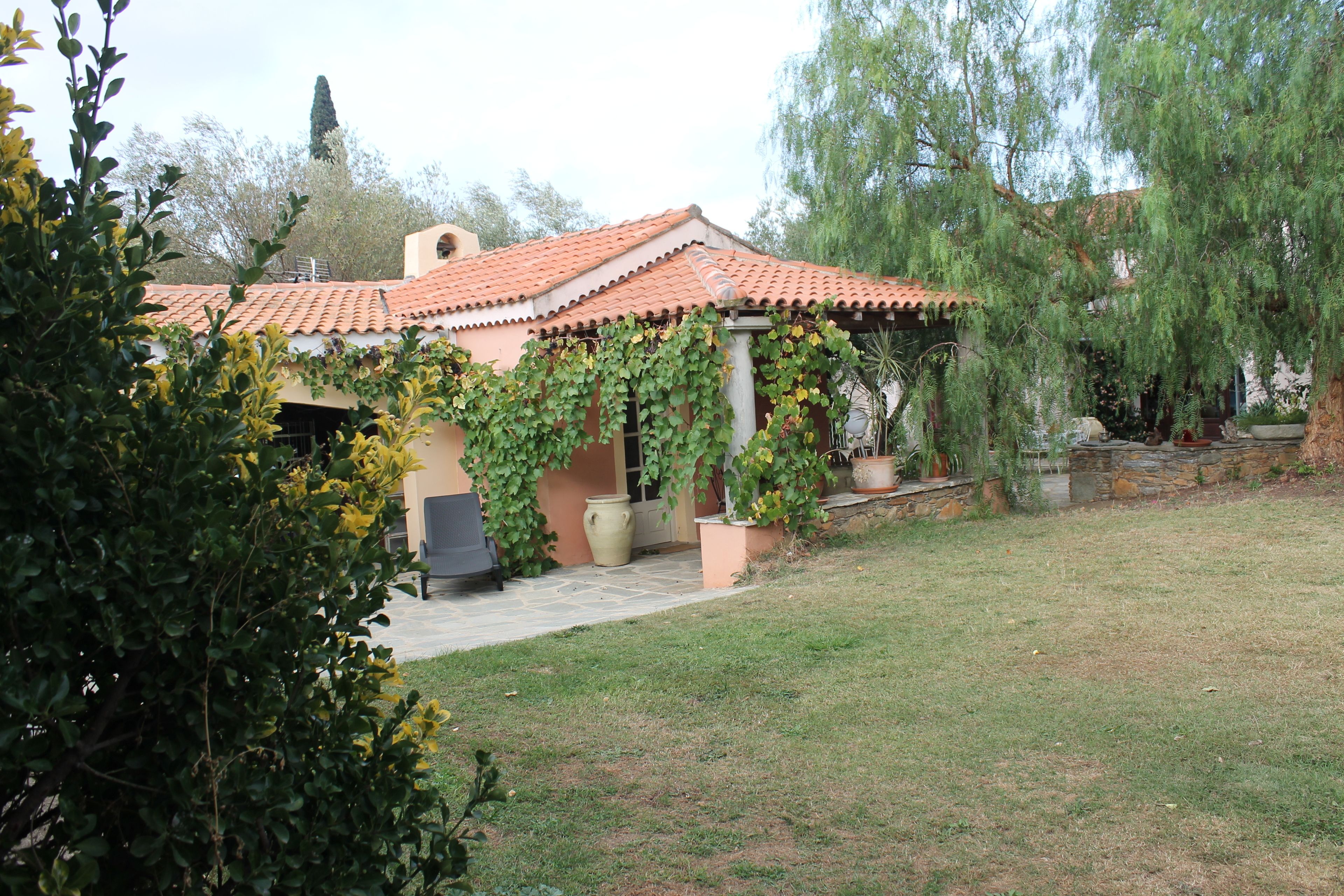 Une maison avec un toit en tuiles, une véranda et un jardin avec une pelouse et des arbres.