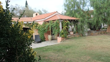 Une maison avec un toit en tuiles, une véranda et un jardin avec une pelouse et des arbres.