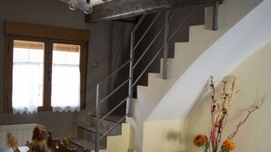 Un comedor con una mesa y sillas de madera, una escalera y un florero con flores.