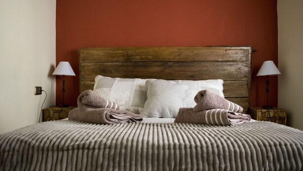 Una cama bien hecha con cabecera de madera, dos lámparas de noche y una colcha estampada.