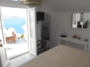A room with a bed, a desk, a chair, a TV, and a view of the sea. - Rimida Villas - Adults Only (Santorini)