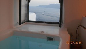 A room with a bathtub and a window with an arched view of the sea and distant mountains. - Rimida Villas - Adults Only (Santorini)