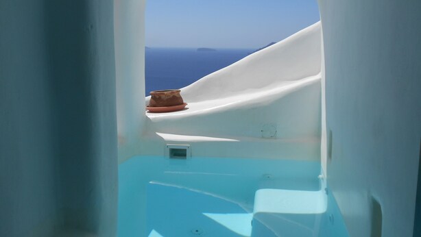 A narrow, white-walled room with a view of the sea and a brown pot on a white surface. - Rimida Villas - Adults Only (Santorini)