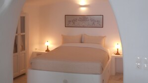 A bedroom with a bed, two bedside tables with lamps, a wall-mounted artwork, and an arched doorway. - Rimida Villas - Adults Only (Santorini)