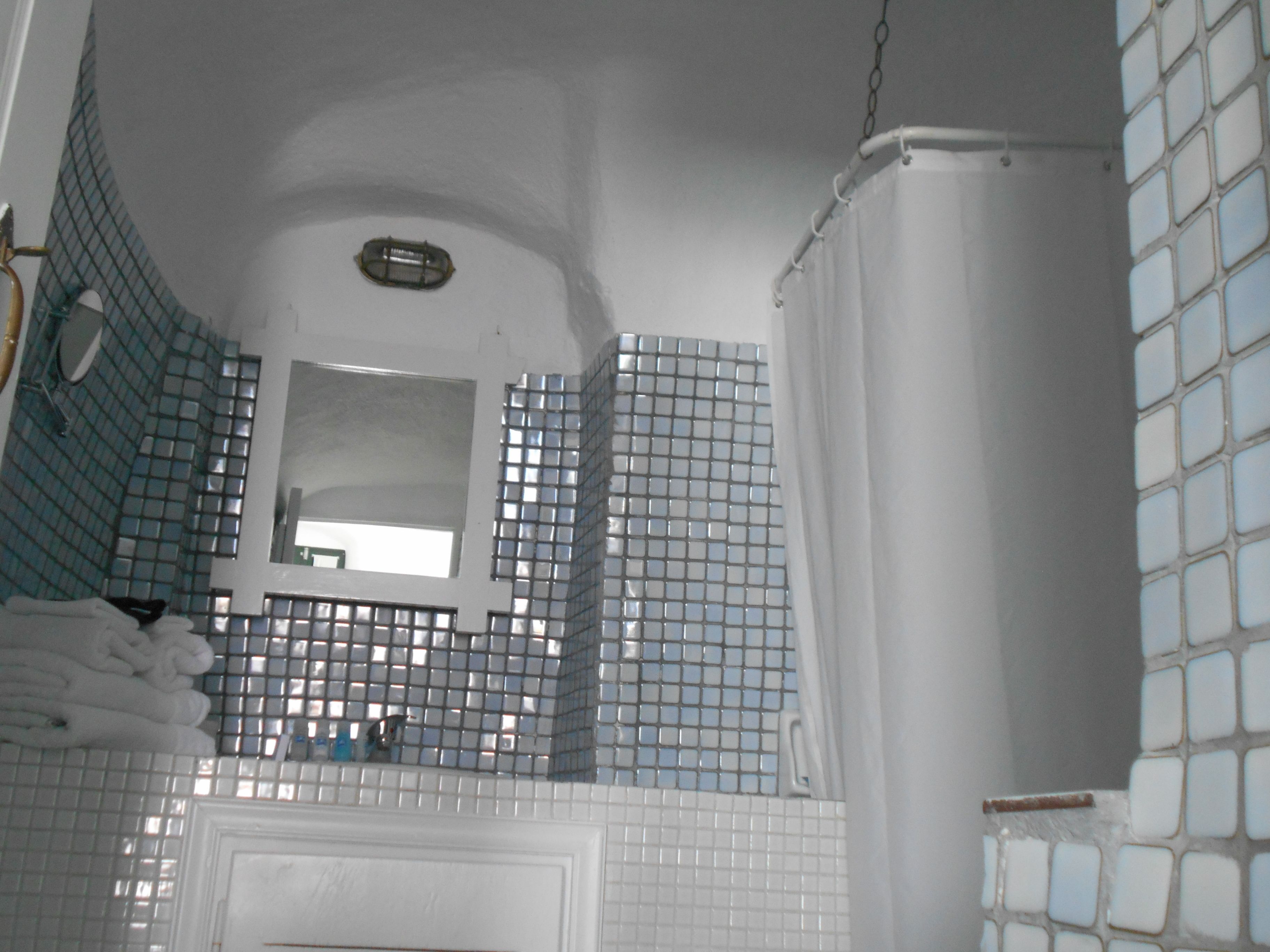 A bathroom with blue-tiled walls, a white bathtub, and a mirror above the sink.