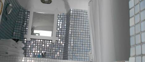 A bathroom with blue-tiled walls, a white bathtub, and a mirror above the sink.