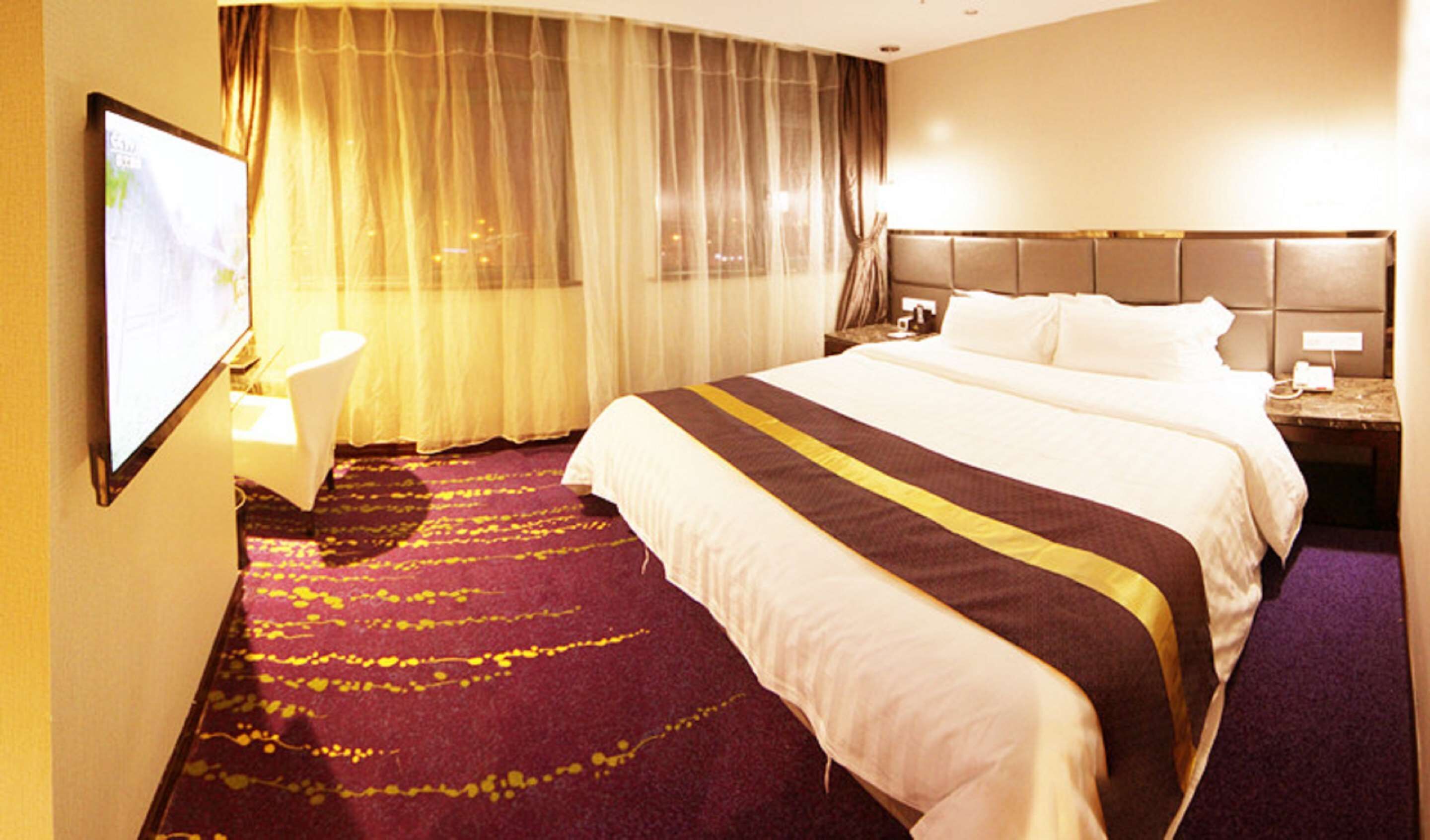 A hotel room with a large bed, a bedside table, a TV, and a bathroom.