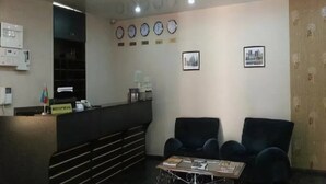 A reception area with a counter, several clocks, framed pictures, and a seating area with chairs and a table. - Boyuk Gala Hotel (Baku)