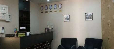A reception area with a counter, several clocks, framed pictures, and a seating area with chairs and a table.