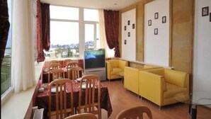 A dining area with a table set for four, a flat-screen TV, and yellow sofas. - Boyuk Gala Hotel (Baku)