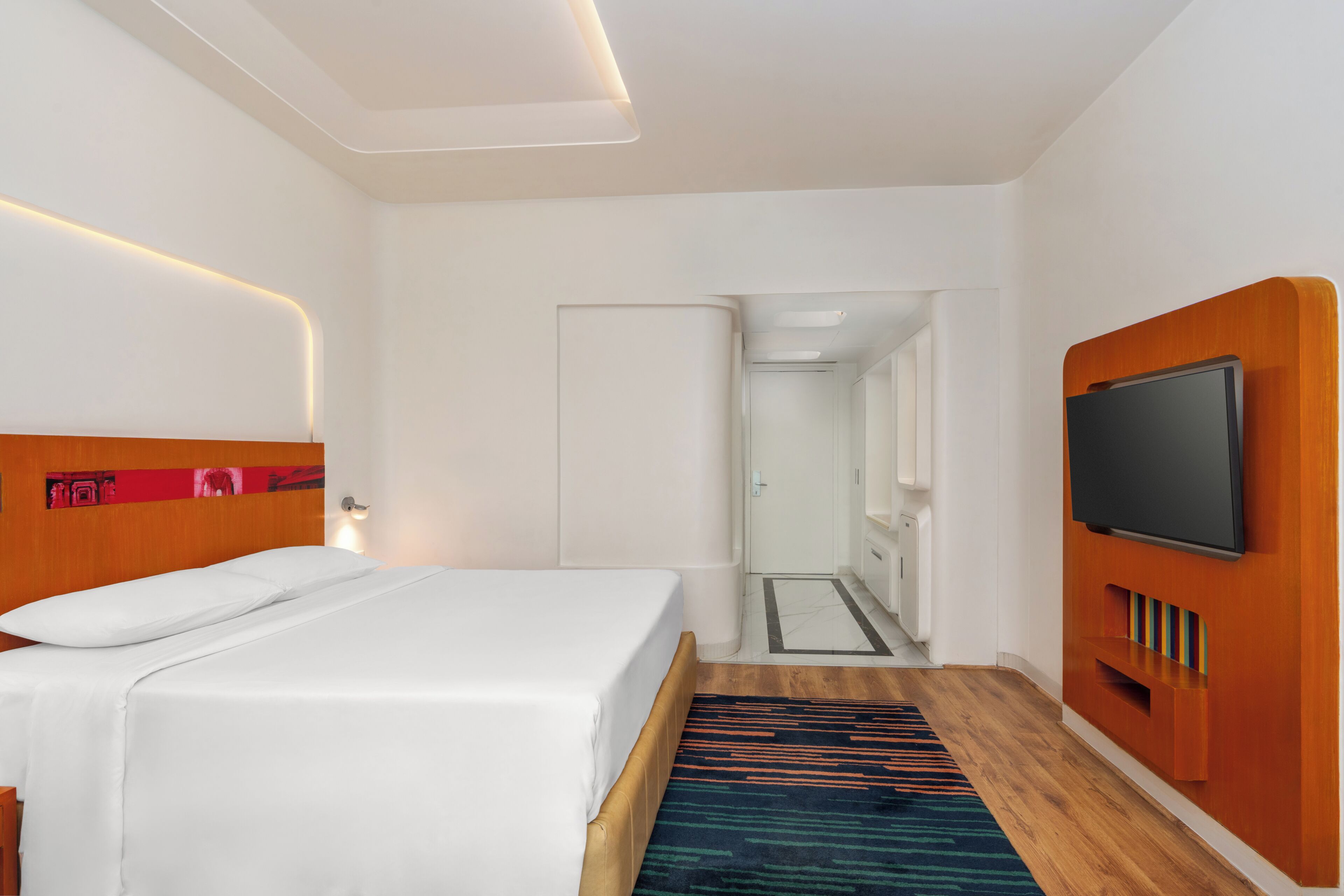 A modern hotel room with a bed, a television, and a bathroom visible in the background.