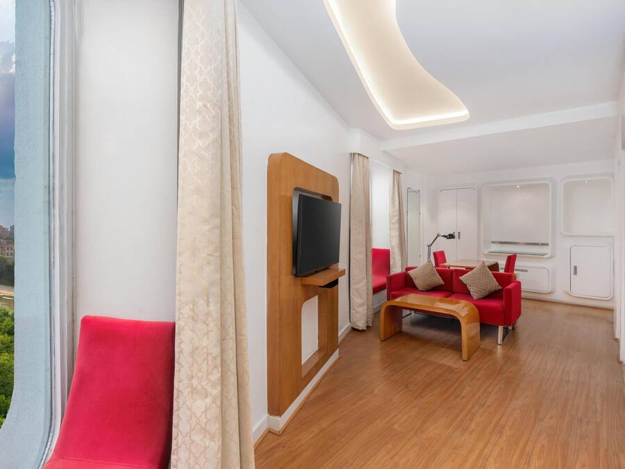 Un salon moderne avec un téléviseur, un canapé rouge et une vue sur la verdure à l’extérieur.